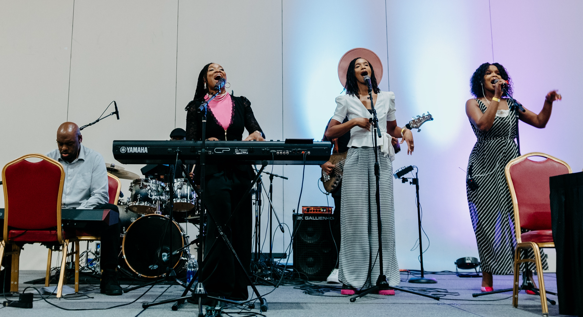 Musicians performing on stage: drummer, keyboardist, saxophonist, and two singers with microphones at CIC