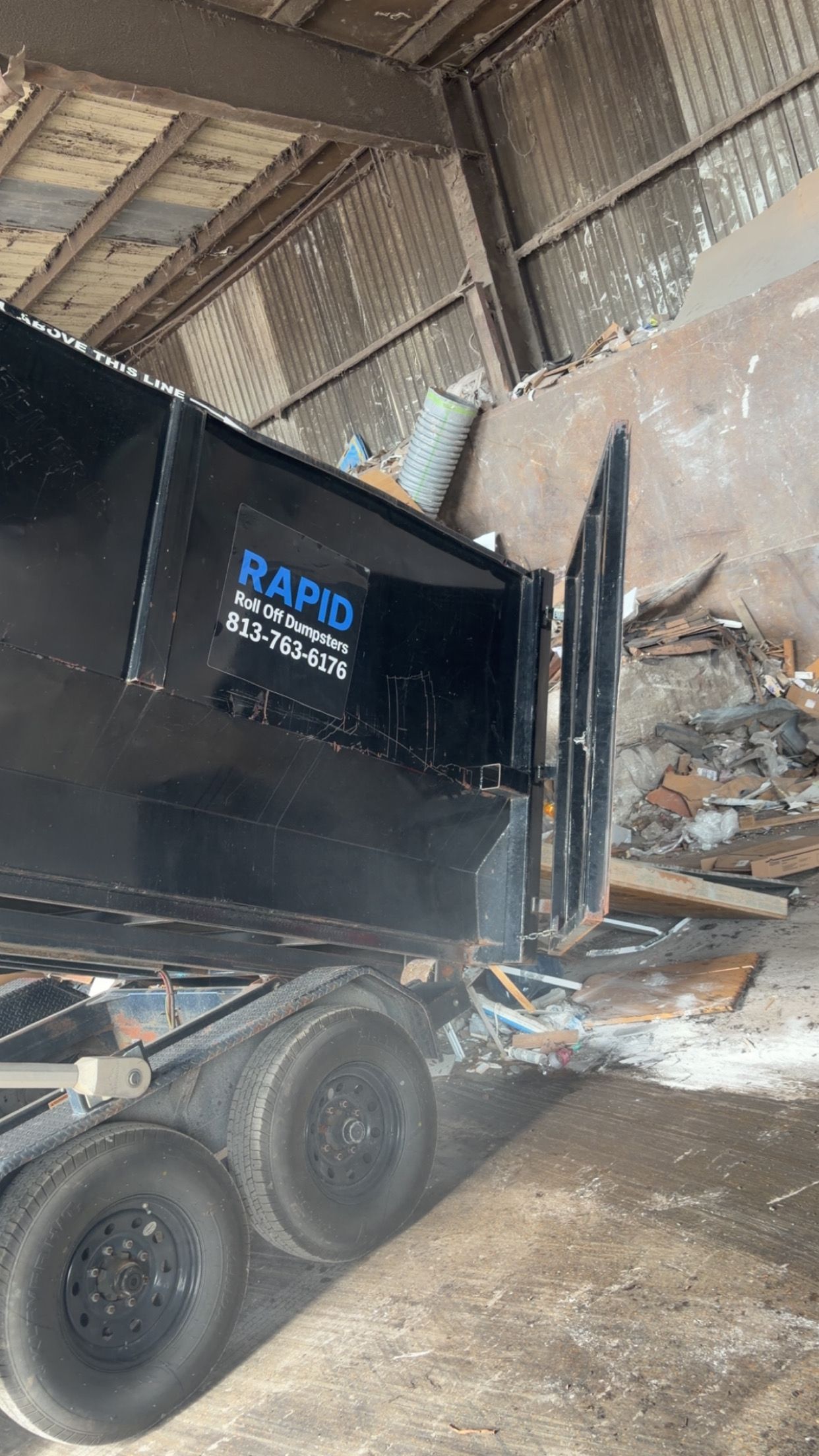 Large black dumpster parked in a driveway in front of a house.