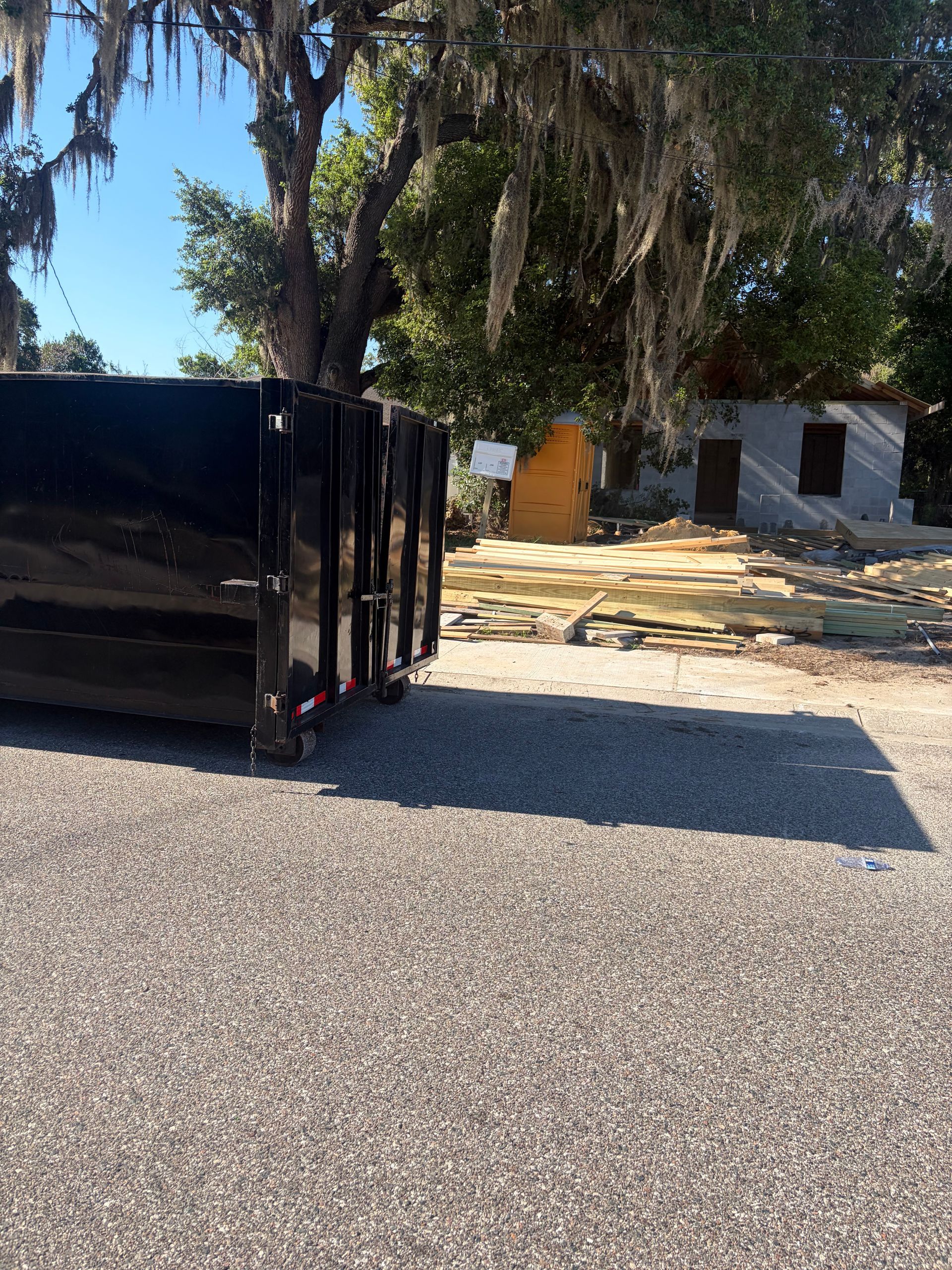 Large orange roll-off dumpster on gravel in a yard, with trees and houses in the background