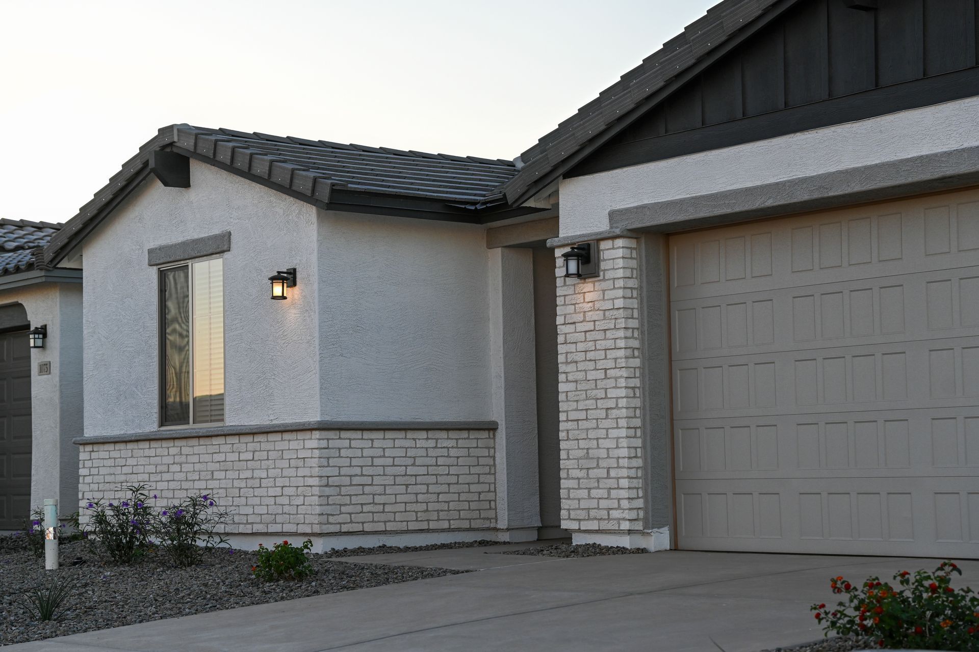 A single-story suburban home with a white stucco facade, light brick accents, a gray tiled roof, and a beige garage.