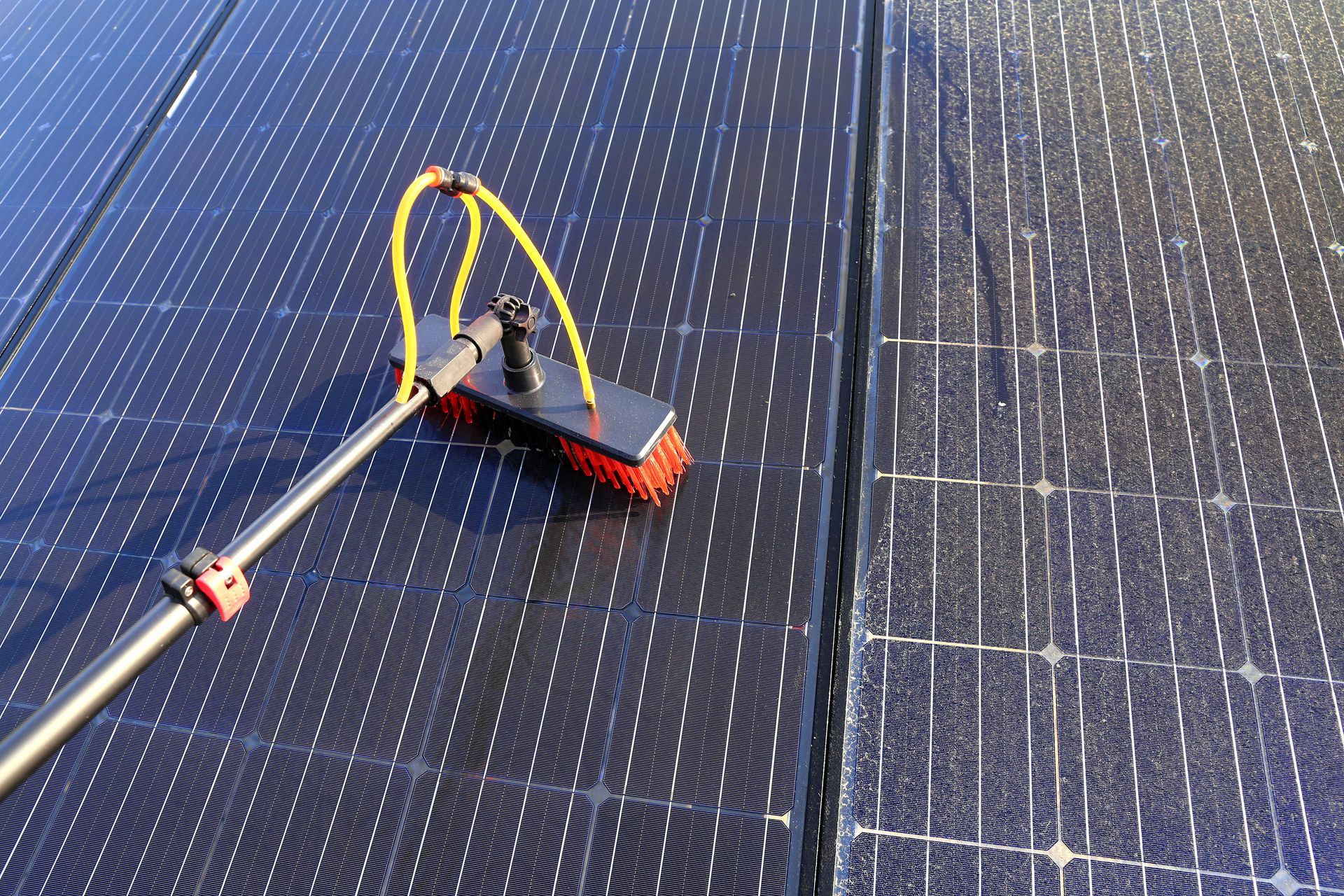 Solar panel cleaning with water-fed brush tool on rooftop photovoltaic system.