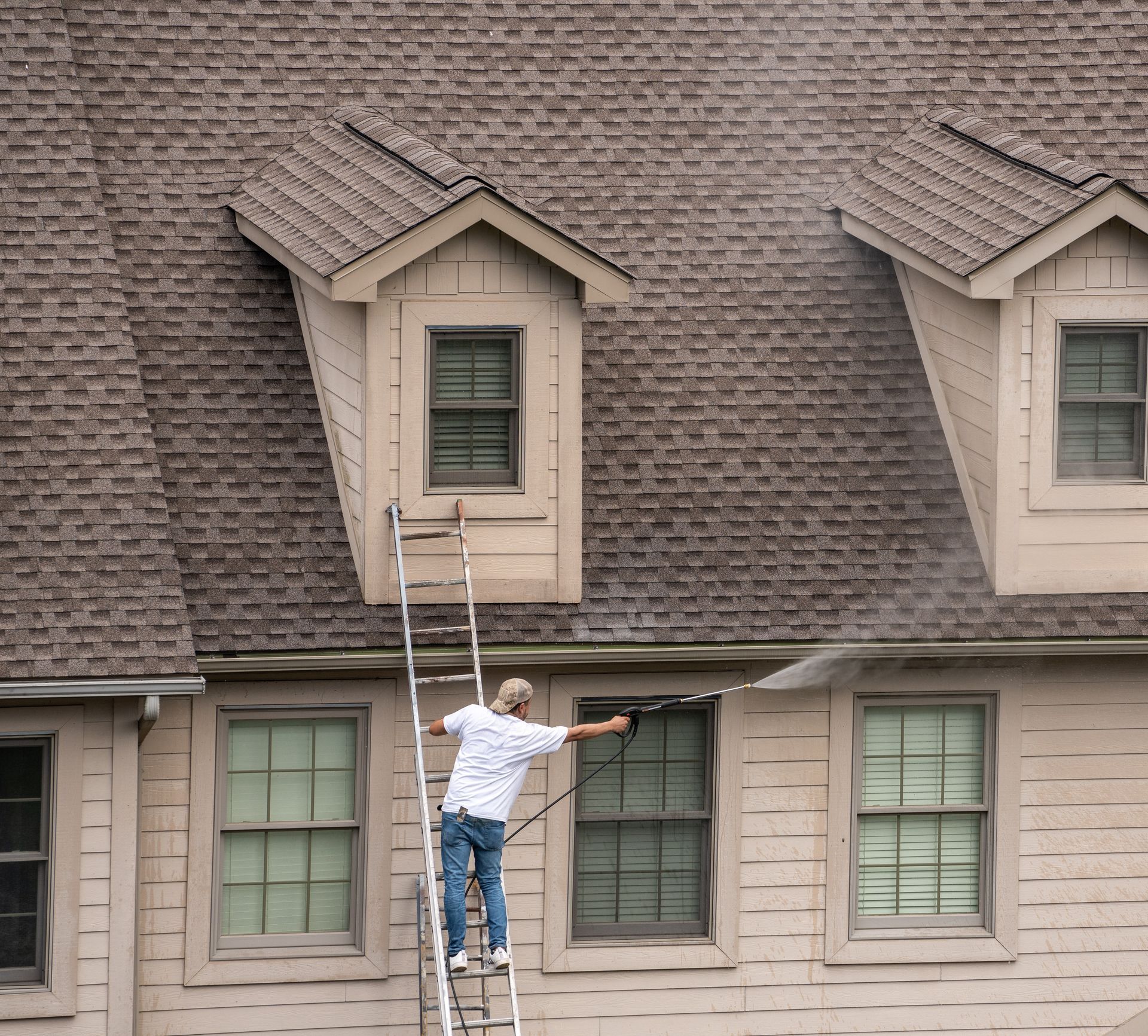 Painter on ladder using pressure wash spray to clean roofing.