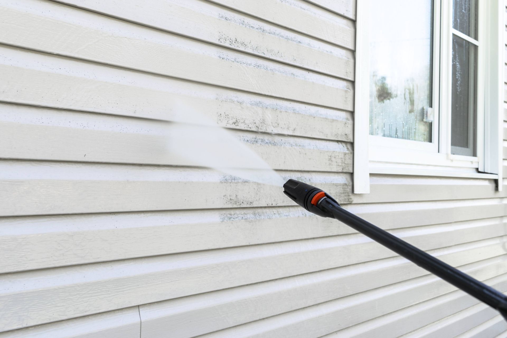 Power washer cleaning siding on a house, removing dirt.