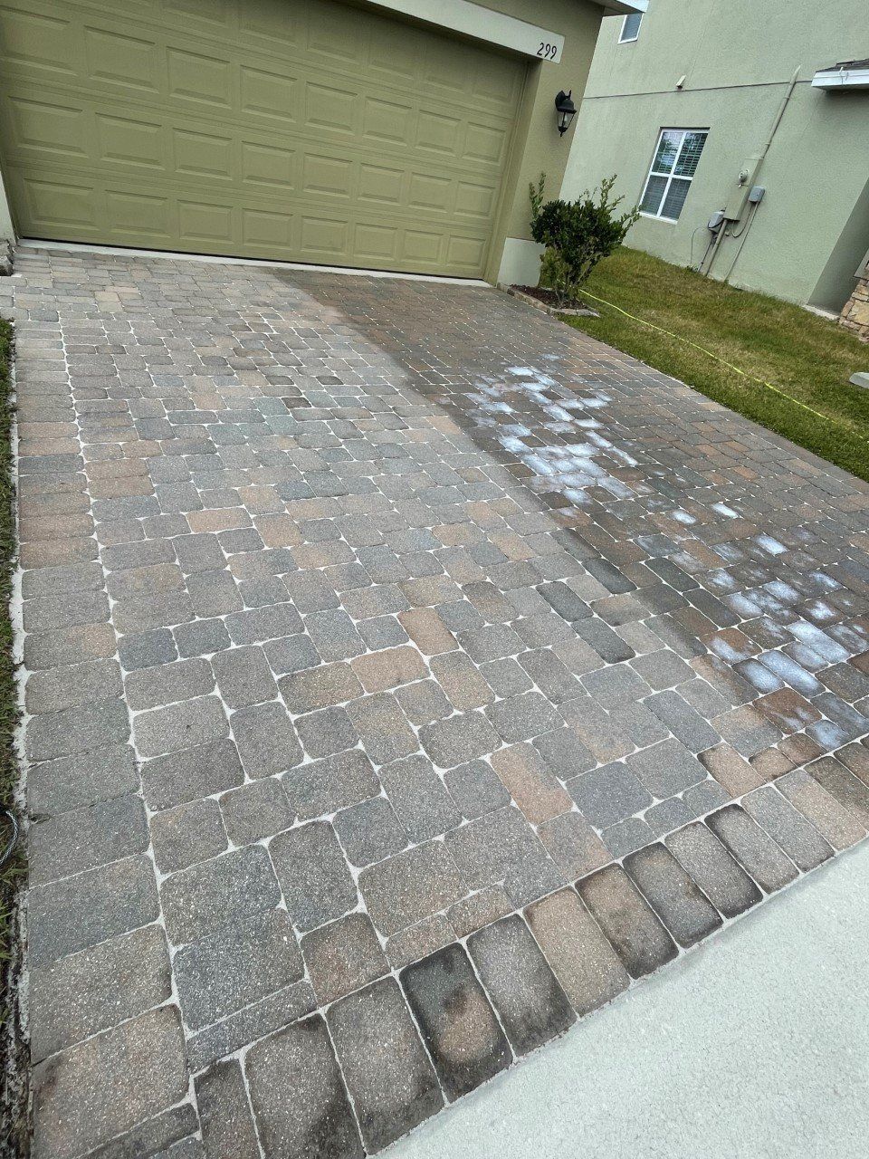 A residential driveway with a partially cleaned paver section next to a weathered, dirty section with white spotting.