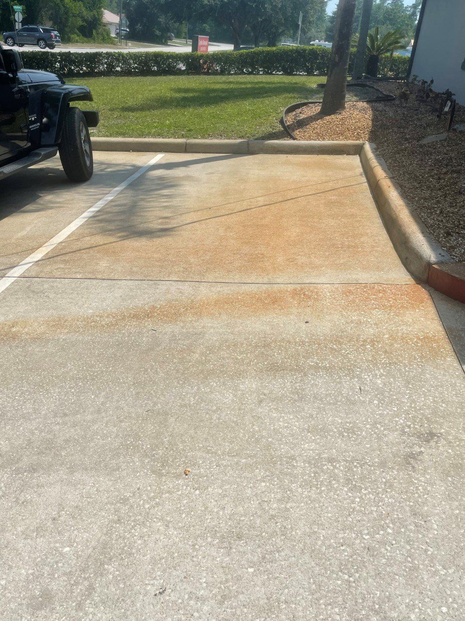 A concrete parking space with orange rust staining, located next to a curb, green grass, and a parked vehicle.