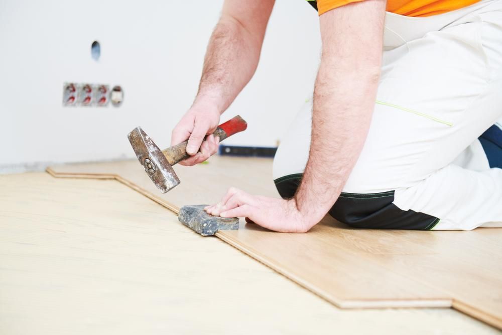 A Man Is Kneeling On The Floor Holding A Hammer — B2B Flooring Solutions In Forster, NSW