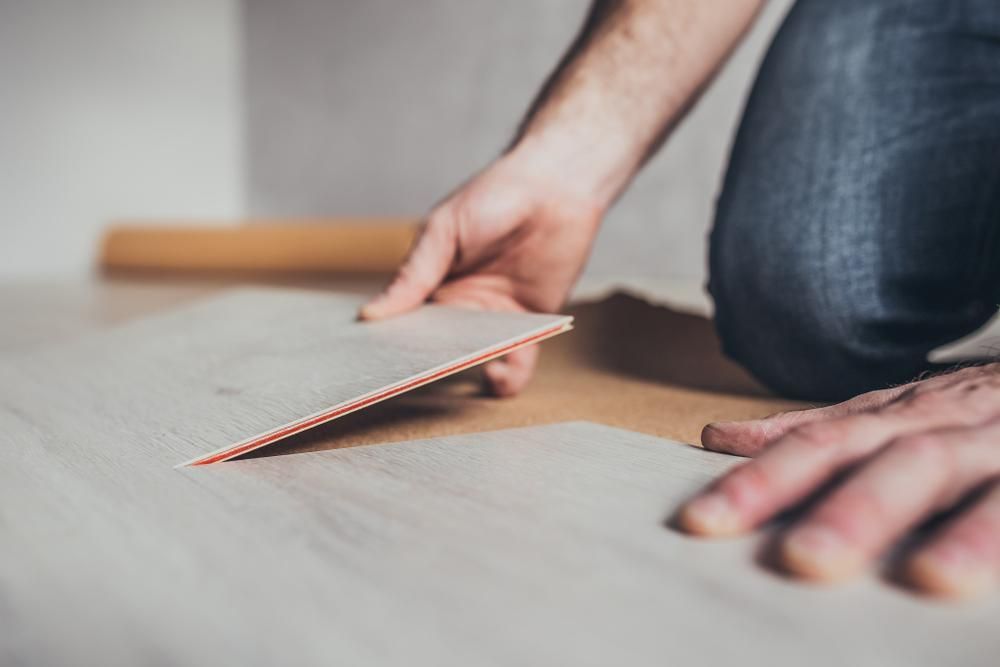 A Man Is Kneeling On The Floor Holding A Piece Of Carpet — B2B Flooring Solutions In Taree, NSW