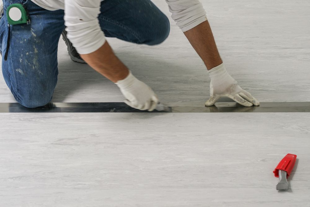 Worker Installing New Vinyl Tile Floor Construction Worker Cut and Stick New Pvc Floor Roll — B2B Flooring Solutions In Coffs Harbour, NSW