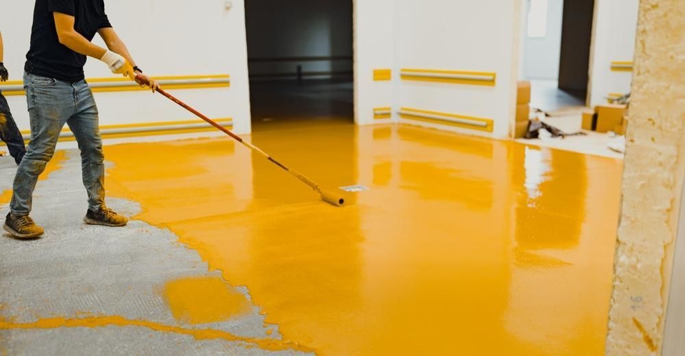A Man Is Painting A Floor With A Roller — B2B Flooring Solutions In Forster, NSW