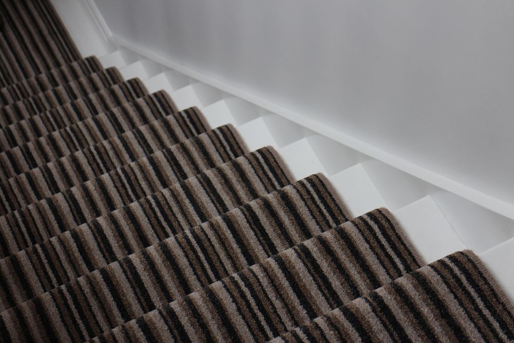 A Close Up Of A Staircase With A Striped Carpet And A White Railing — B2B Flooring Solutions In Kempsey, NSW