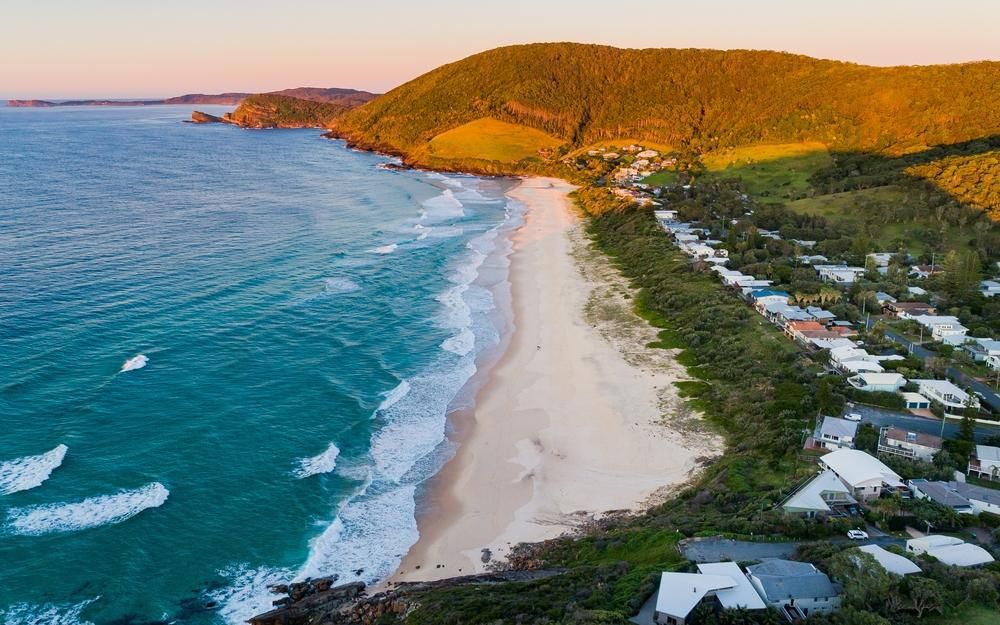 An Aerial View Of A Beach With Houses And Mountains In The Background — B2B Flooring Solutions In Mid North Coast, NSW