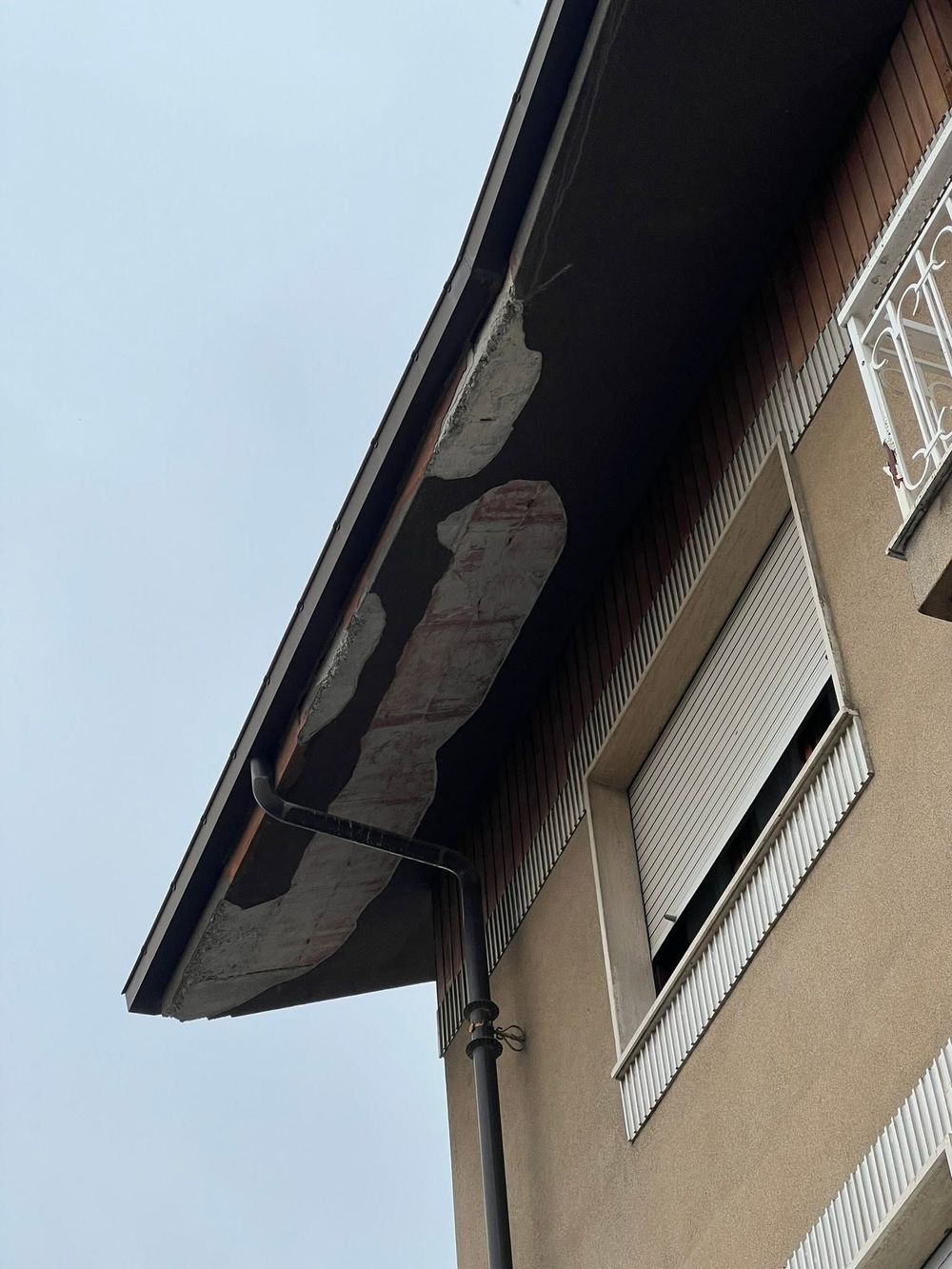 Due persone su una piattaforma elevatrice accanto a un edificio, lavorano sul balcone più alto sotto un cielo azzurro e nuvoloso.