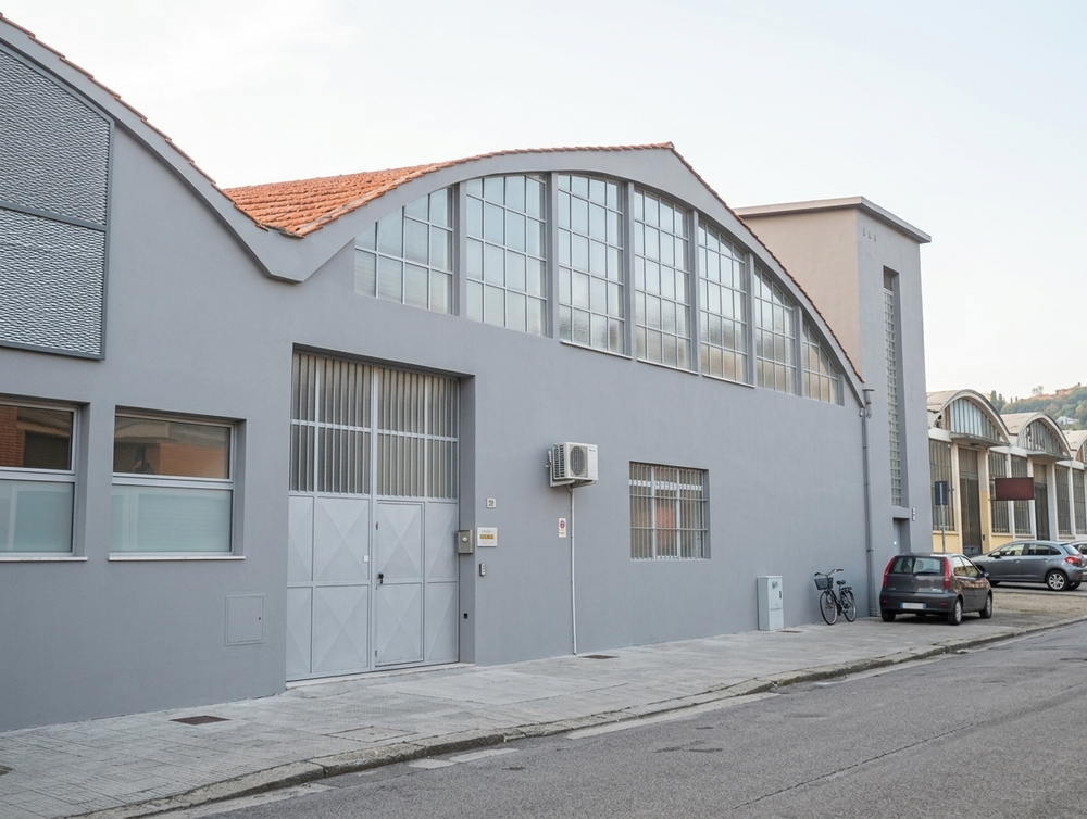 Un'autogru solleva una struttura in legno accanto a un edificio coperto da impalcature e reti, lungo una stretta strada sterrata.