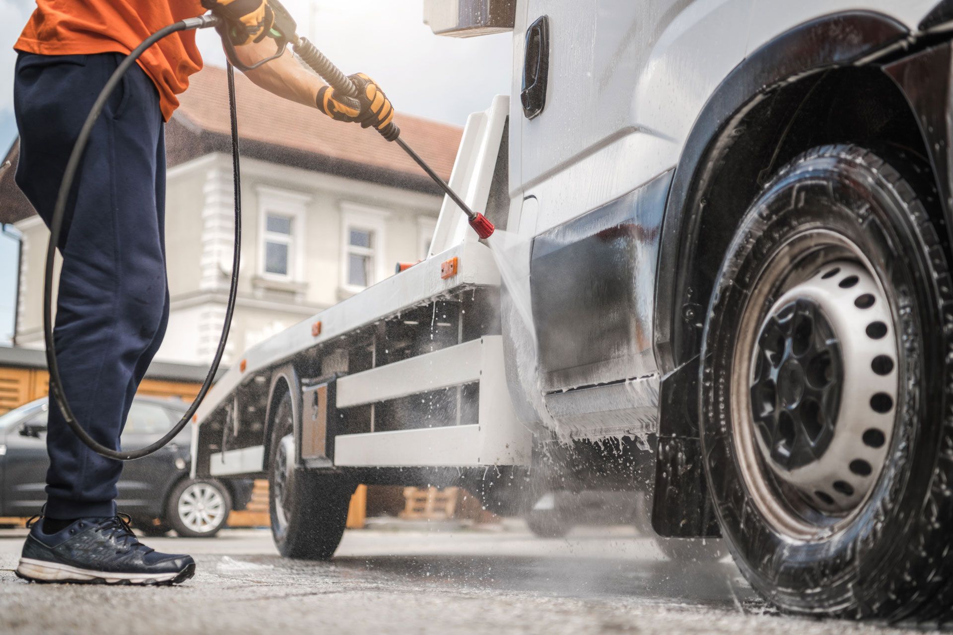 Person washing a white tow truck with a pressure washer outdoors.
