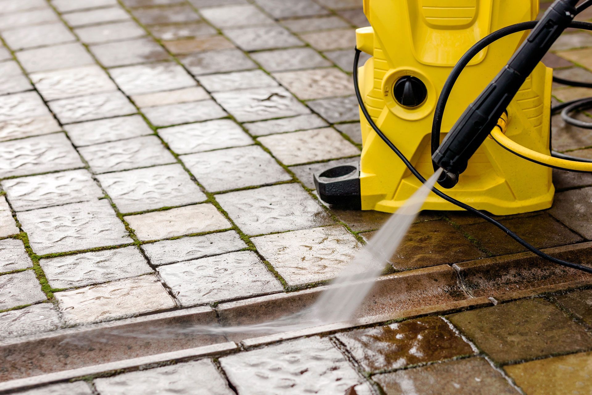 Yellow pressure washer cleaning brick patio.