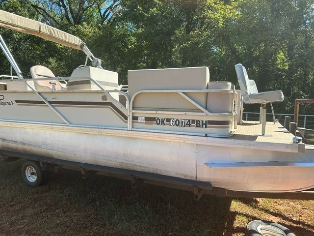 Pontoon boat on trailer, outdoors. Beige, tan, and white. CA registration on side.