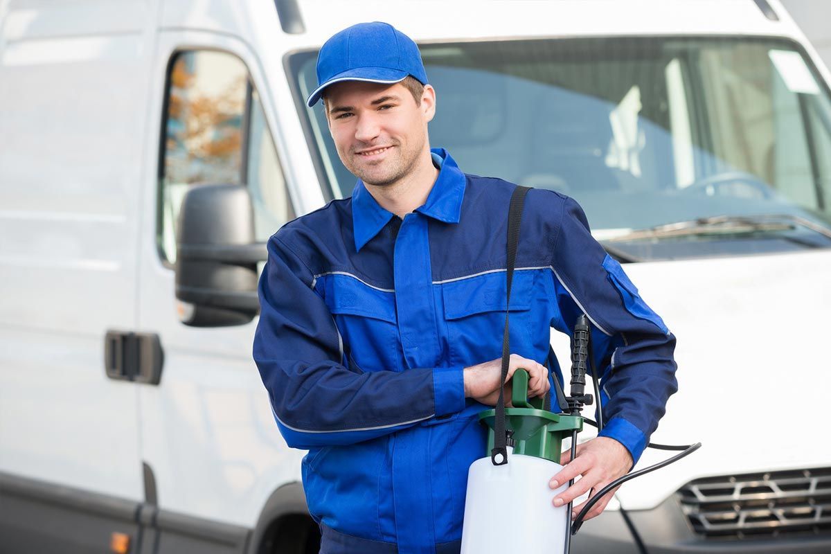 Man in blue uniform with sprayer, standing near a white van.