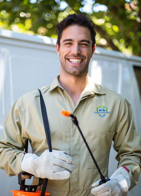 Man in tan workwear smiling, holding a sprayer, standing in front of a van.