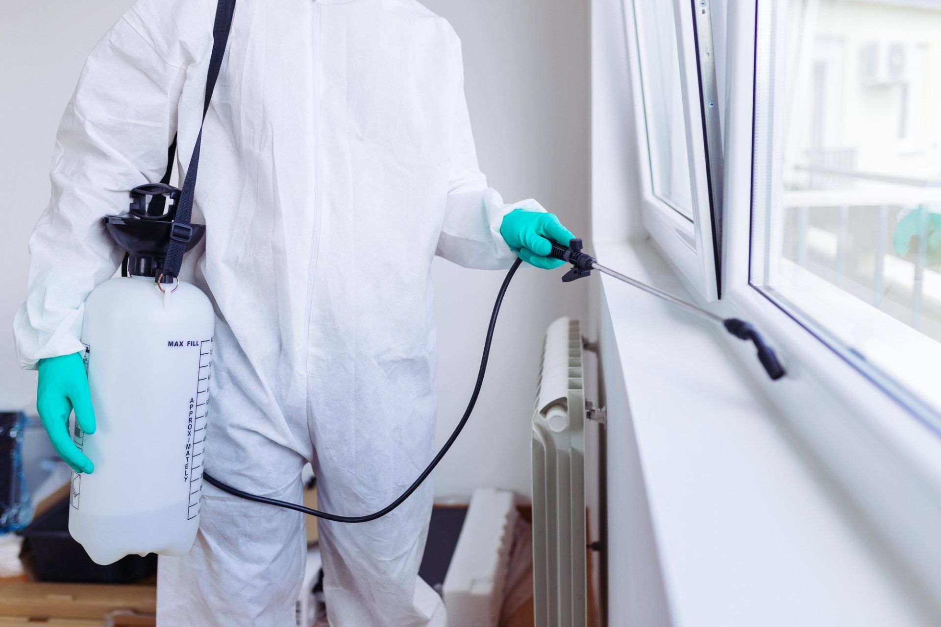 Person in protective suit spraying insecticide near a window.