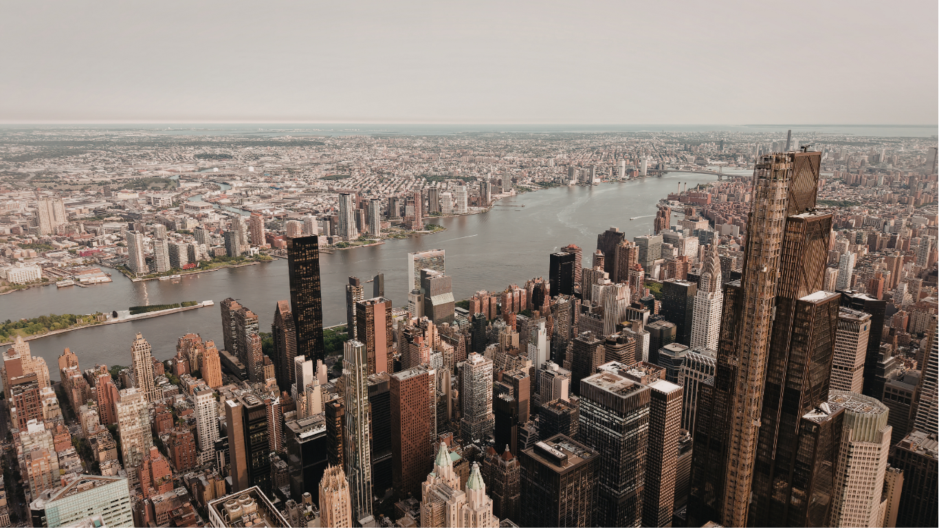 Aerial view of New York City, numerous skyscrapers, a river, and hazy sky.