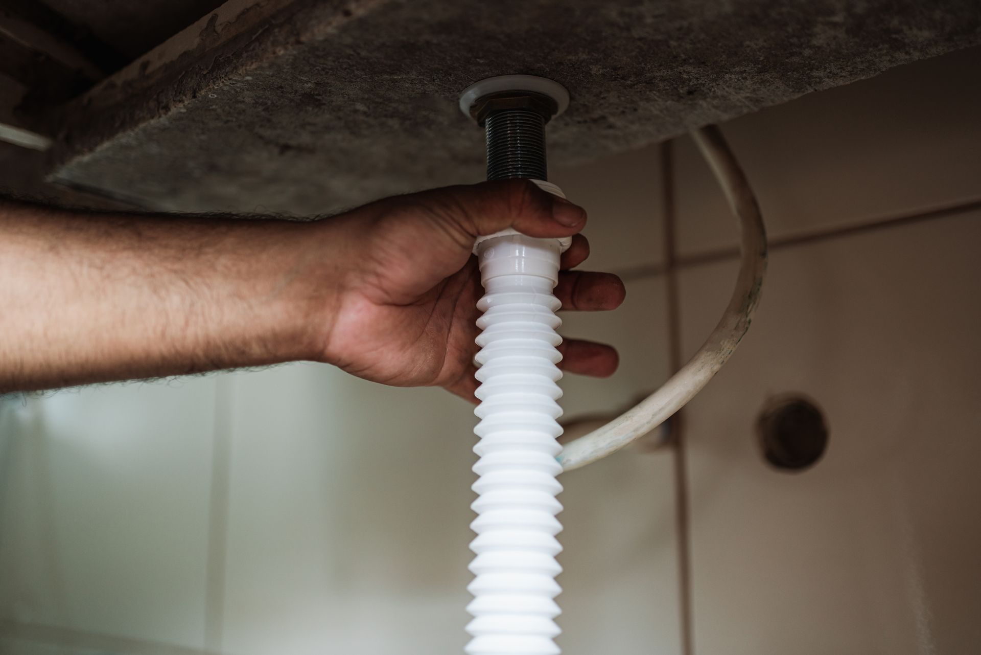 A person is fixing a drain pipe in a bathroom.