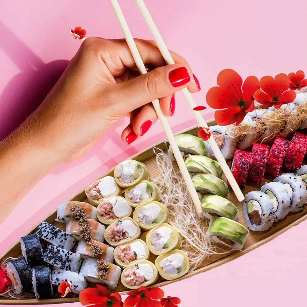 Una persona sostiene palillos sobre un plato de sushi.