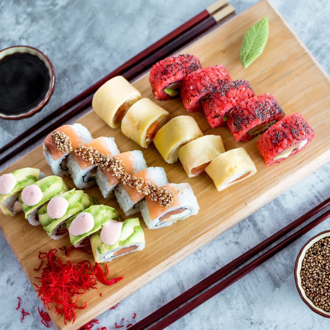 Una tabla de cortar de madera cubierta con sushi y palillos.