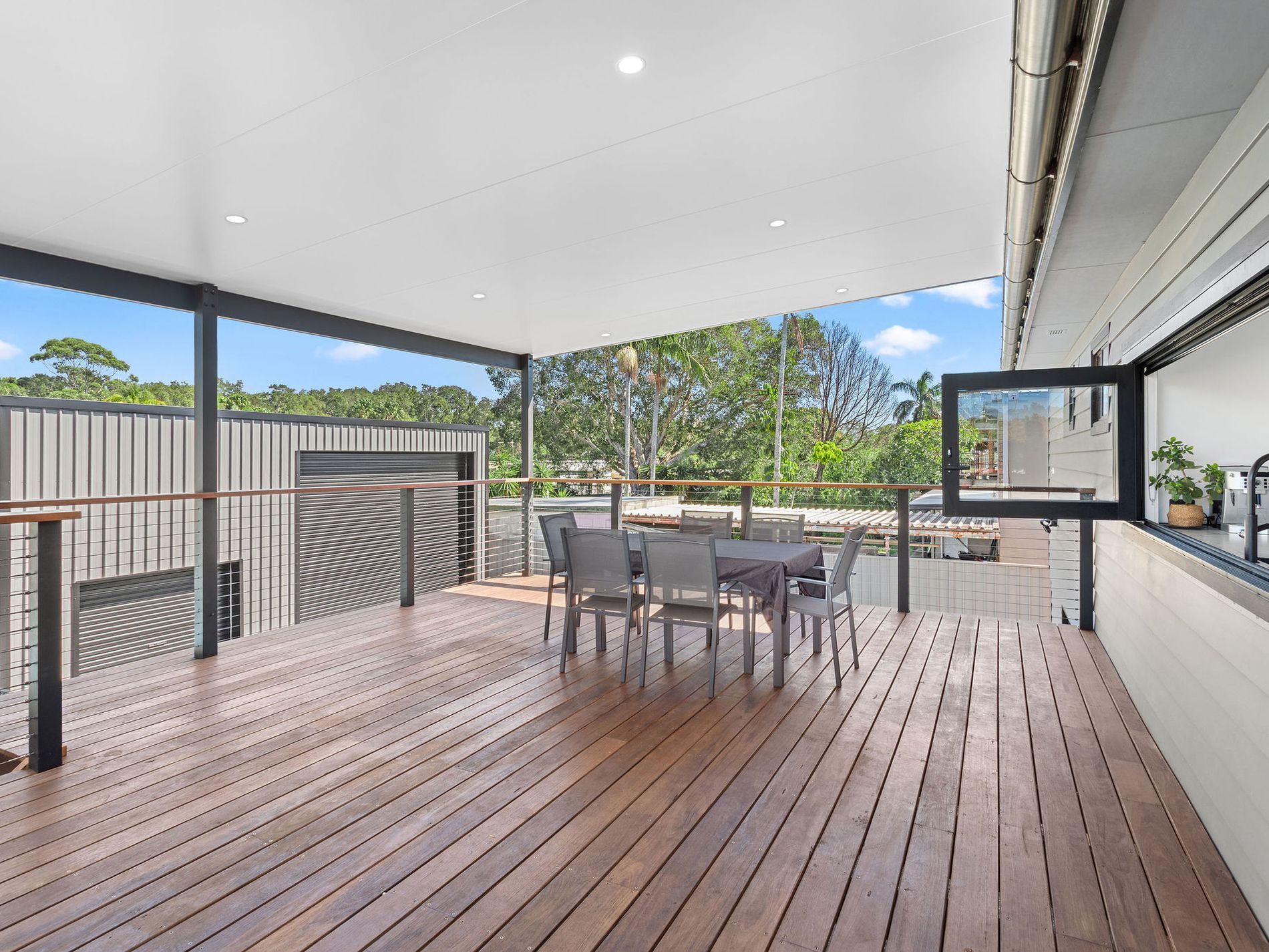 Covered outdoor deck with dining table, wooden flooring, and a view of trees — Wade Adams Constructions in Forster, NSW