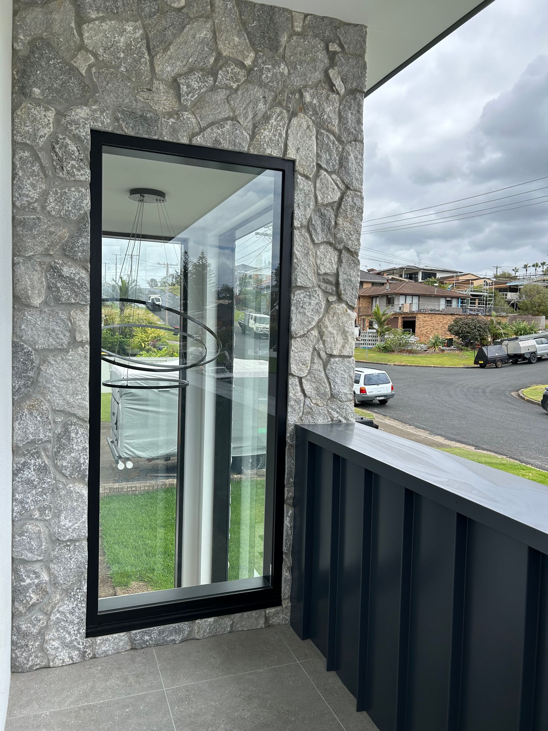 Stone balcony with open black-framed glass door, overlooking a street and hillside homes — Wade Adams Constructions in Forster, NSW