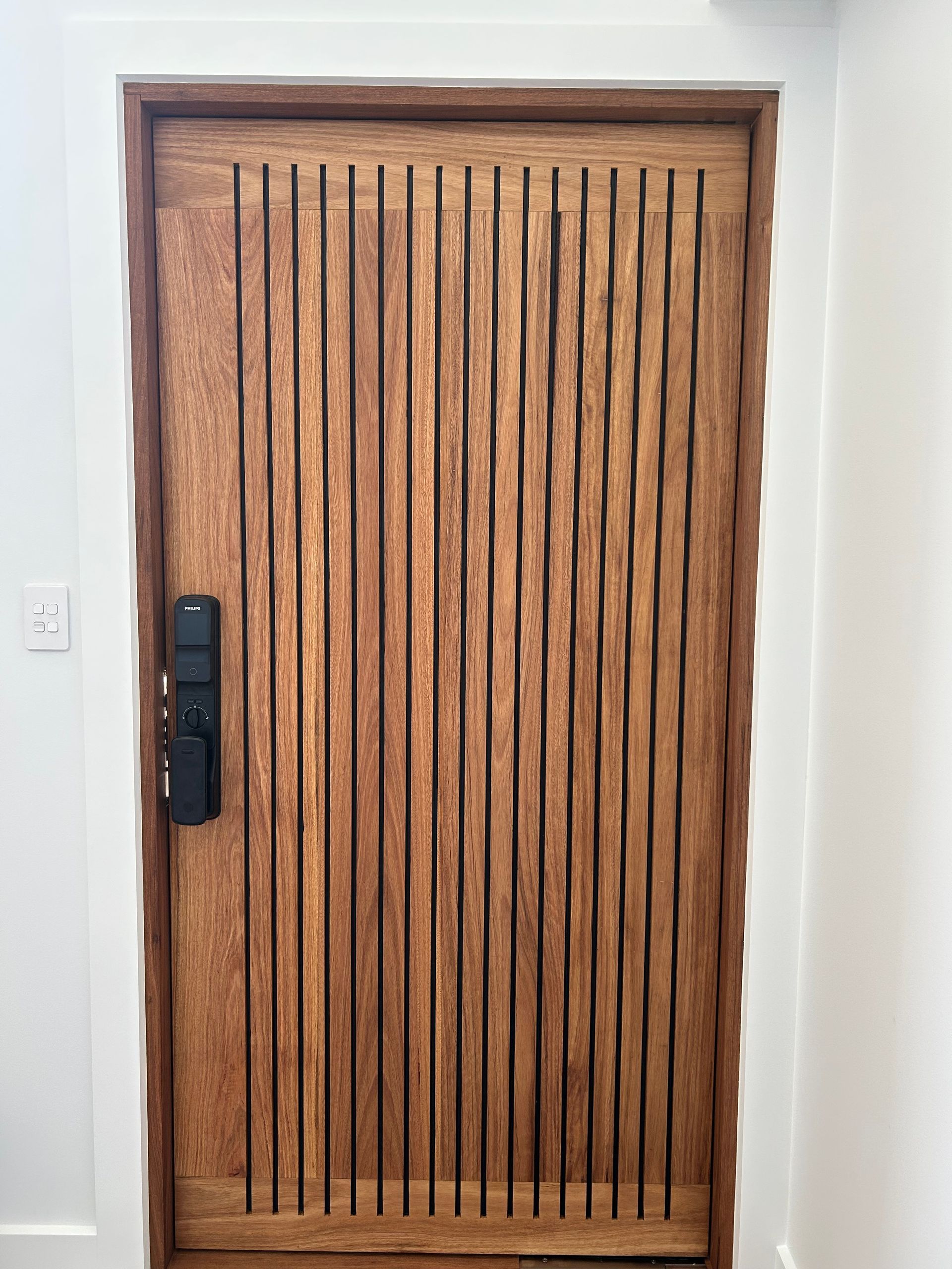 Wooden front door with vertical slats and a black handle, set in a white wall — Wade Adams Constructions in Forster, NSW