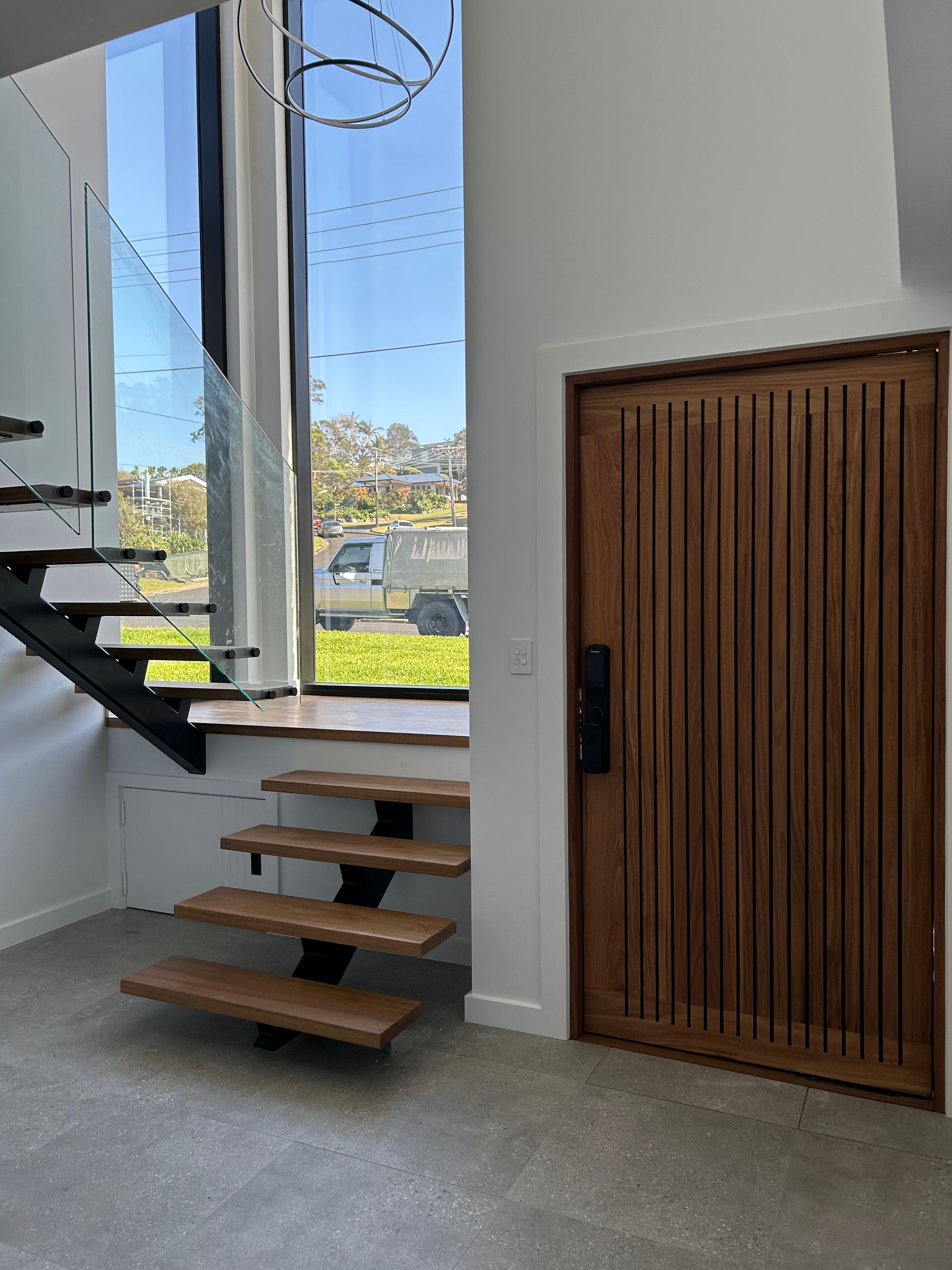Modern staircase and wood slatted door in a bright interior with large windows — Wade Adams Constructions in Forster, NSW