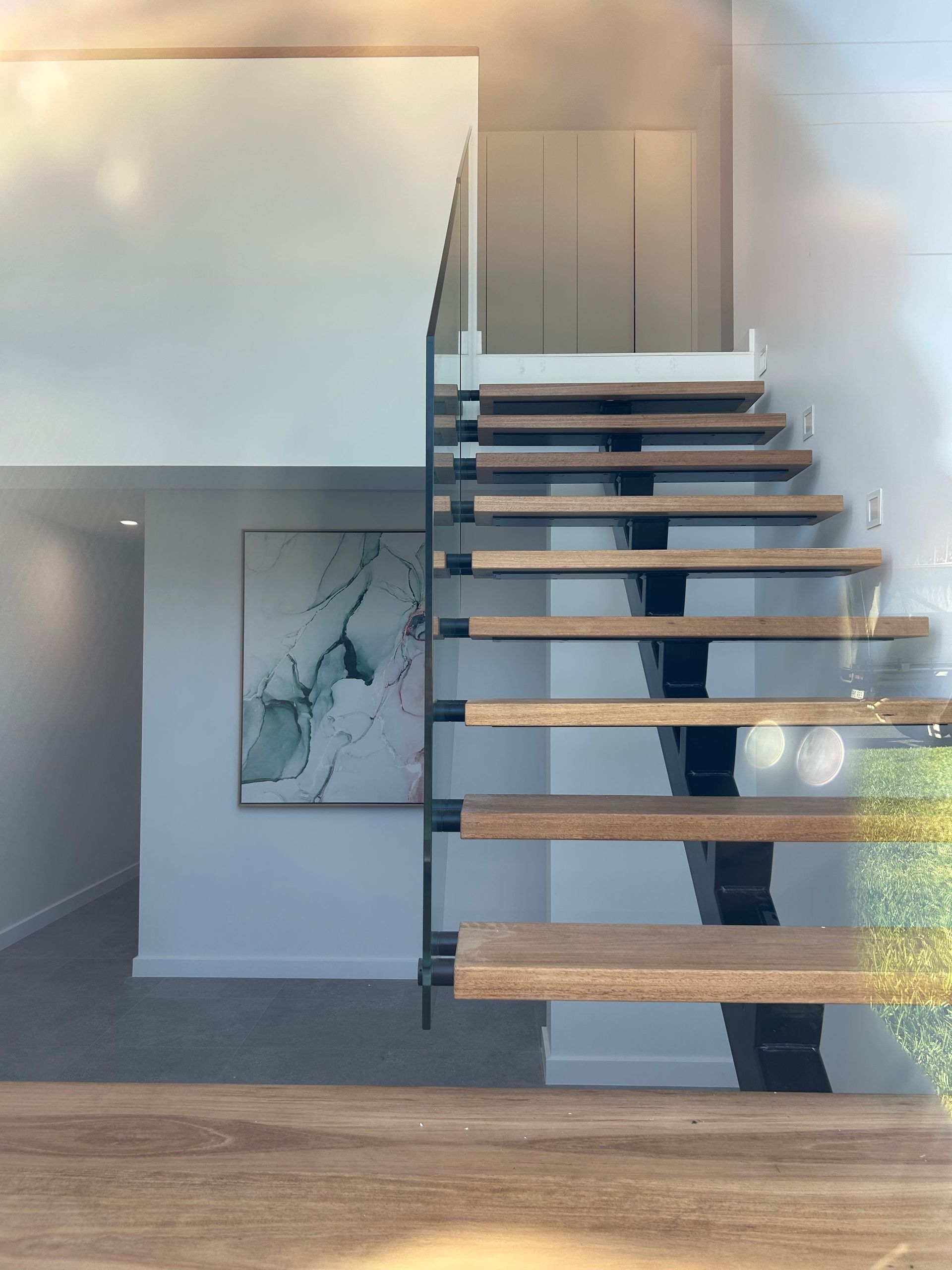 Modern staircase with floating wooden steps and glass railing in a bright minimalist interior — Wade Adams Constructions in Forster, NSW