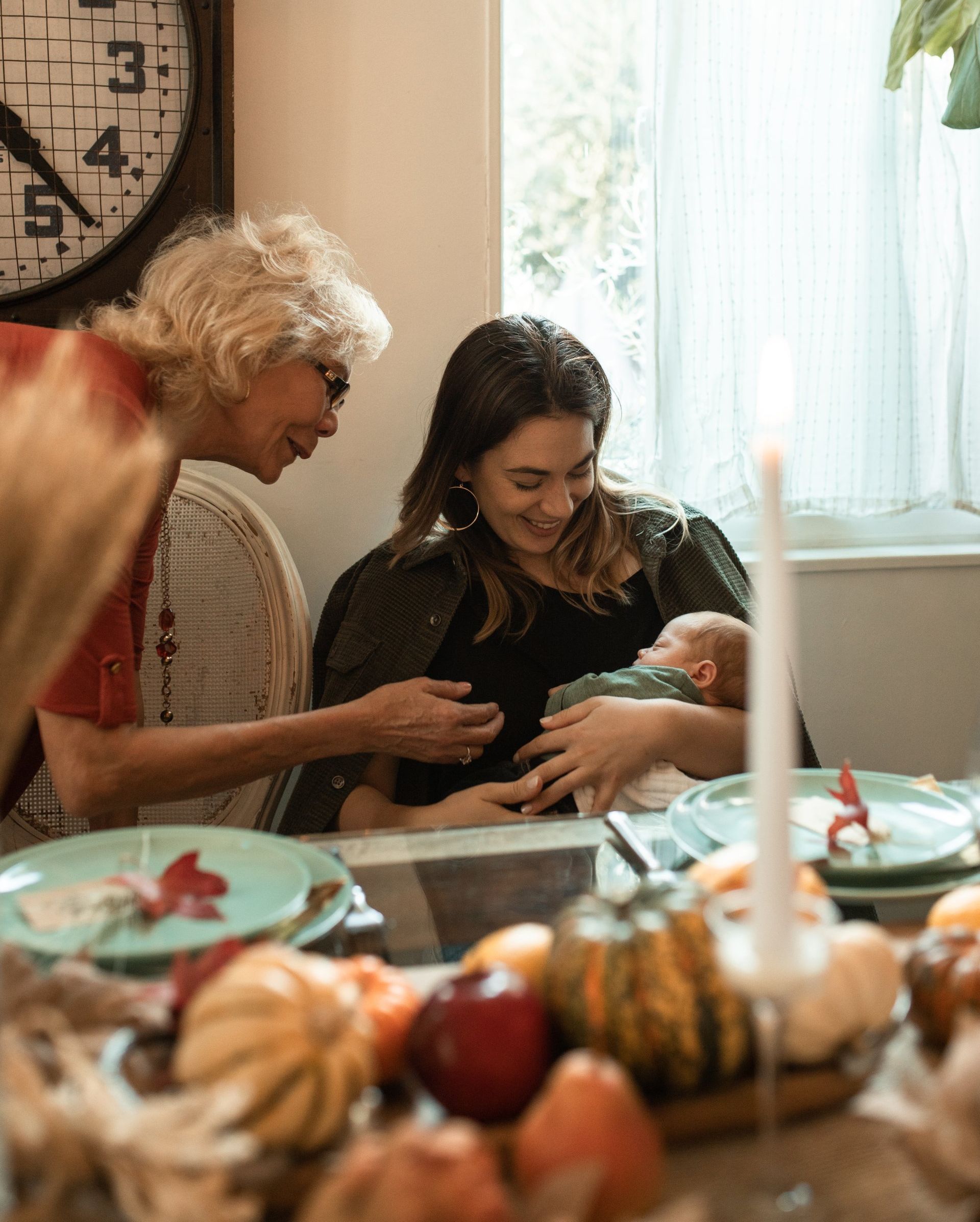 A woman is holding a baby while sitting at a table with other people.