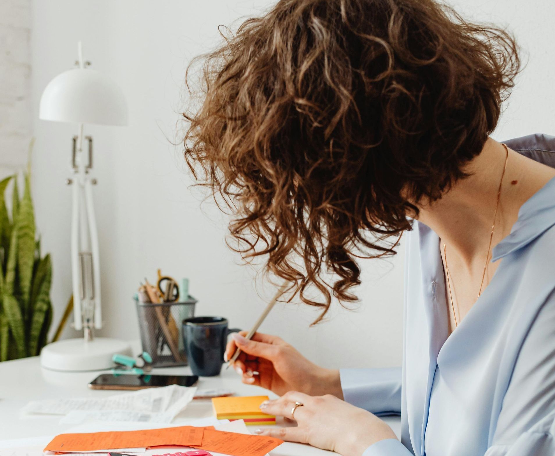 A woman with curly hair is sitting at a desk writing on a piece of paper.