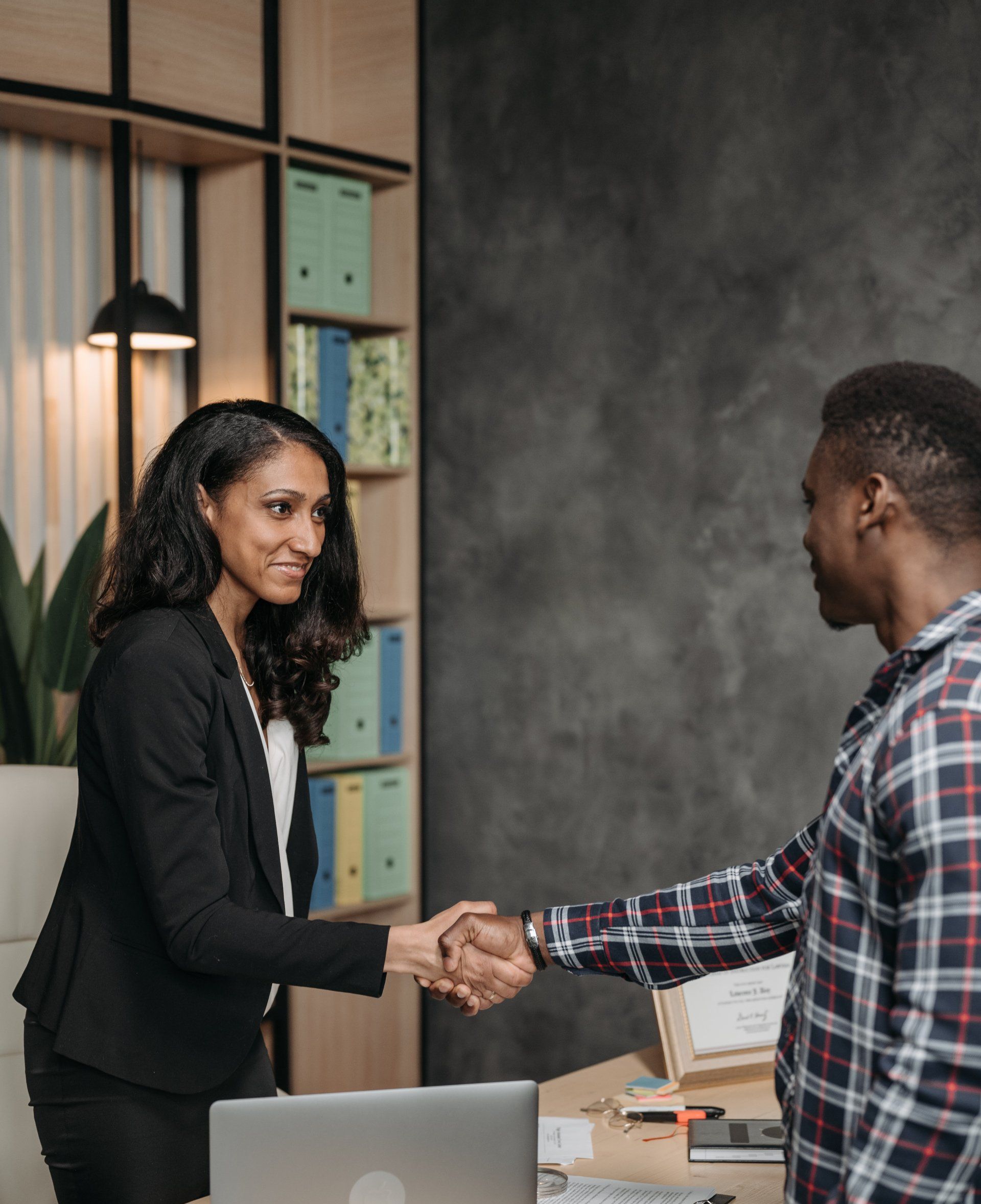 A man and a woman are shaking hands in an office.