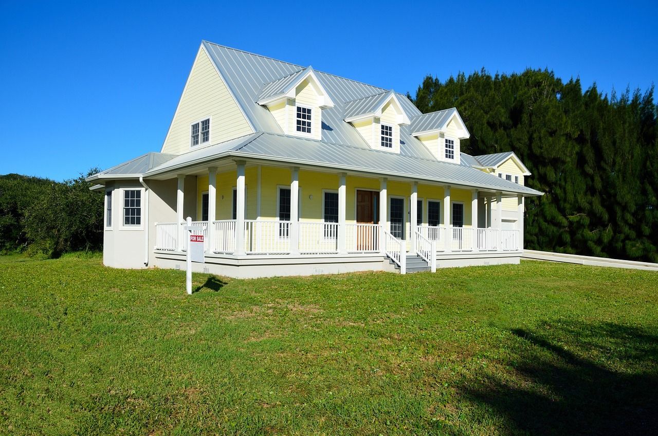 a large white house with a porch and a for sale sign in front of it