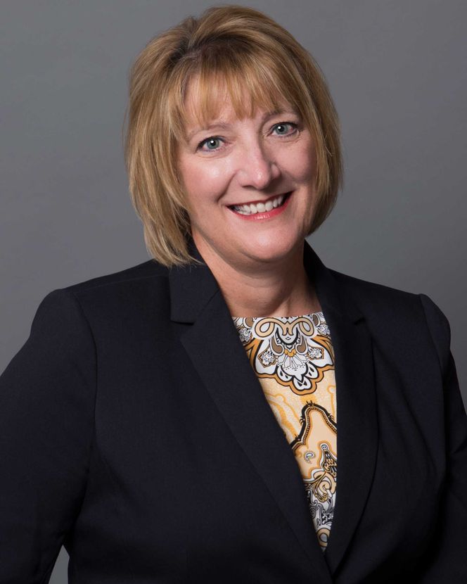 Carolyn Ostovich — Wichita Falls, TX — Ostovich & Associates Smiling professional in a dark blazer with a patterned blouse against a gray background