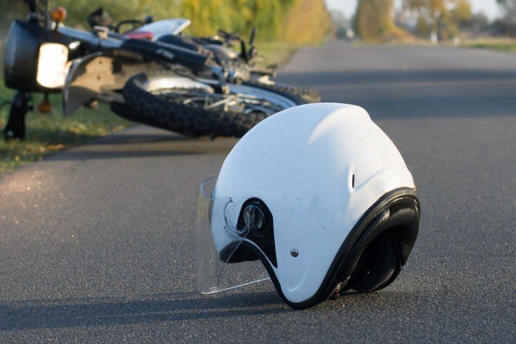 White motorcycle helmet on the road with a blurred motorcycle in the background after a crash