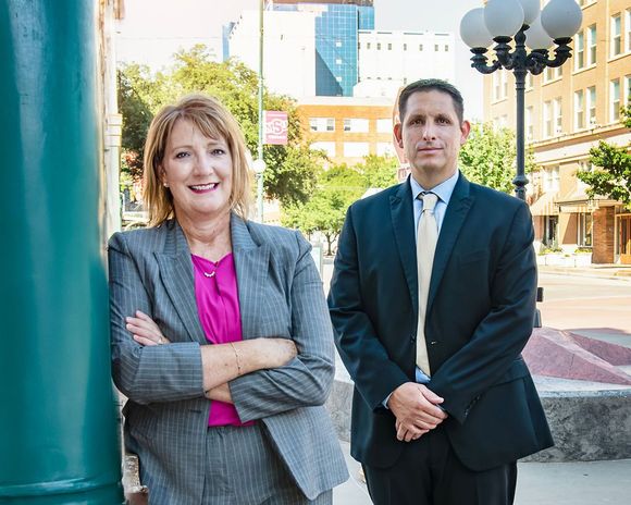 Carolyn And David — Wichita Falls, TX — Ostovich & Associates Two professionals standing outdoors in a city plaza, one in a gray suit and pink blouse, one in a black suit