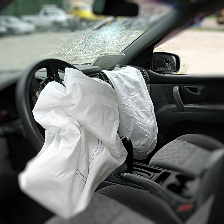 Deployed white airbags inside a car with a cracked windshield and damaged interior