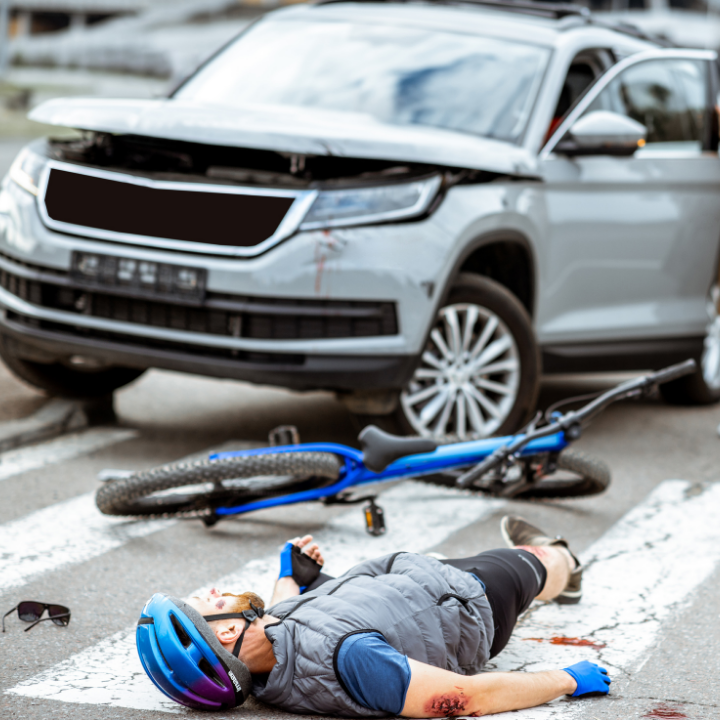 Bicycle crash scene with overturned blue bike and an injured person lying in front of a damaged silver SUV