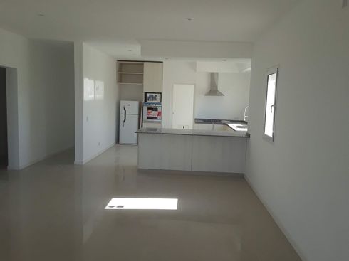 Cocina y sala de estar modernas y vacías, con paredes blancas, suelo de baldosas claras y una ventana luminosa.