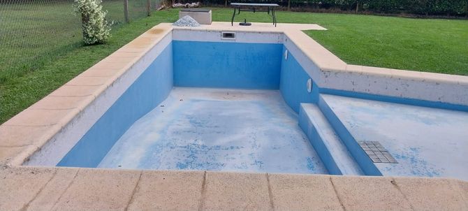 Piscina rectangular vacía con interior azul claro, rodeada de pavimento beige y césped verde.