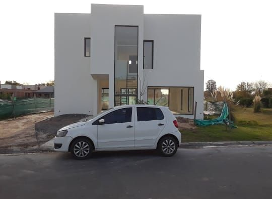 Un coche compacto blanco aparcado delante de una casa blanca moderna con grandes ventanales centrales.