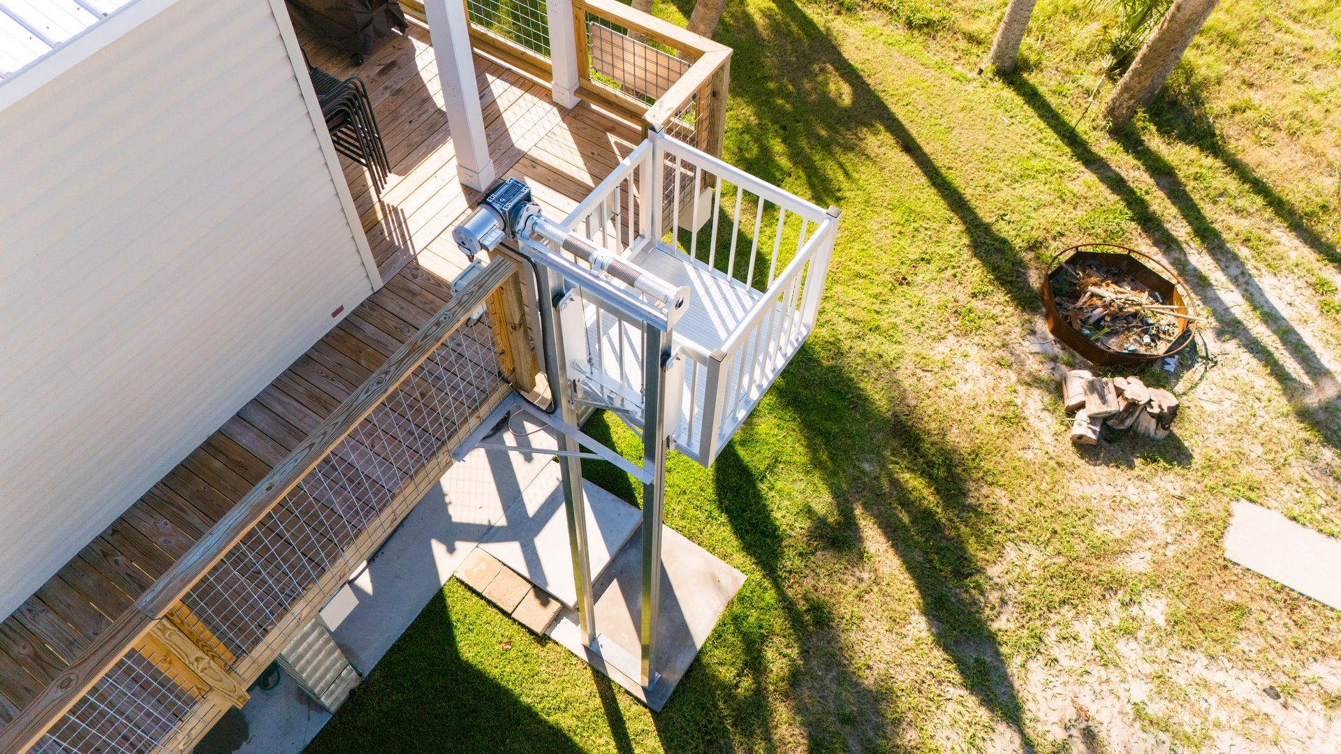 Outdoor residential lift for accessibility next to a house with a wooden deck and green grass.