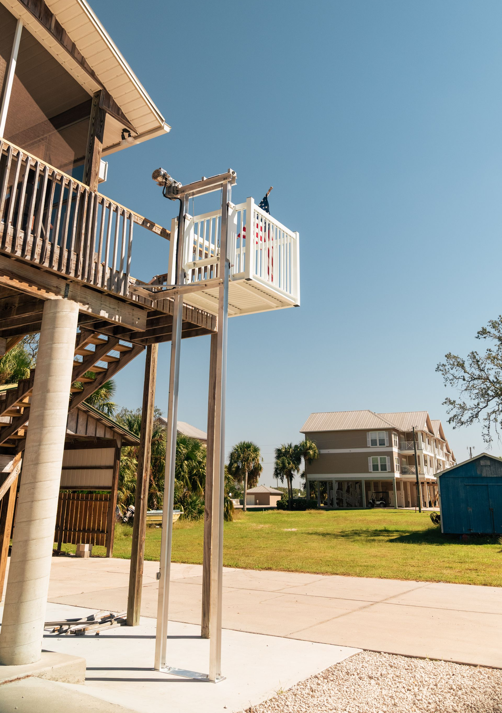 A wheelchair lift on a raised house, with a clear blue sky and other houses in the background.