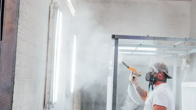 Person spray painting a wall inside a room, wearing a respirator and protective gear.