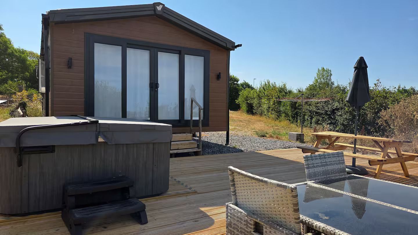 Backyard patio with hot tub, outdoor seating, and a small modern cabin with glass doors and deck.