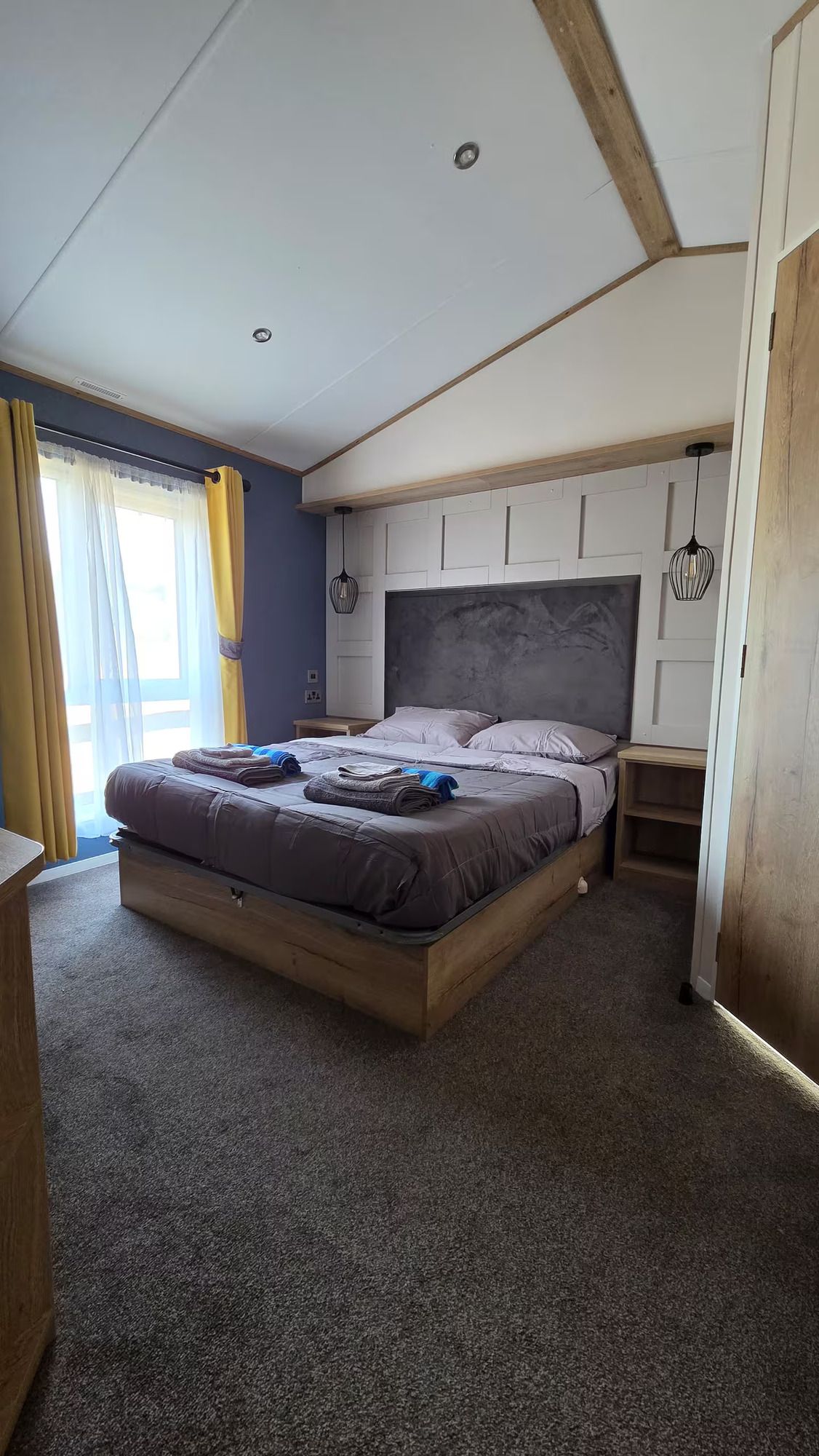 Cozy bedroom with a large bed, sloped ceiling, and sunlight through a window with curtains.