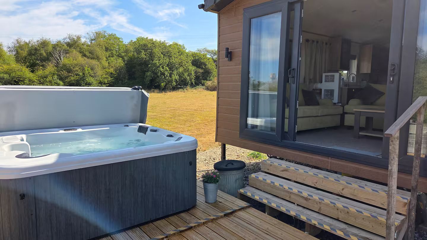Backyard deck with hot tub beside a house and glass doors, overlooking a grassy yard